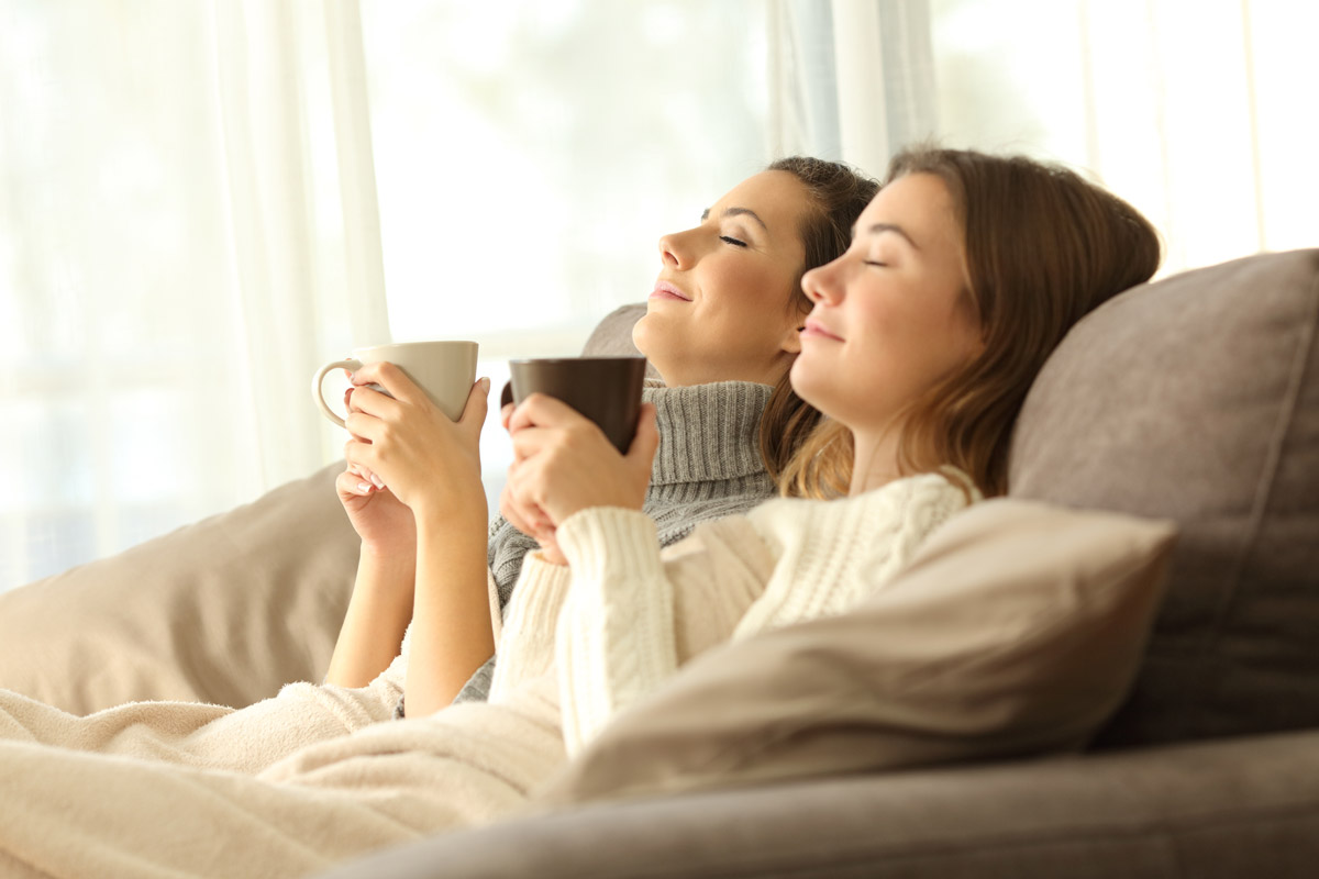 Two women sitting under blanket with coffees