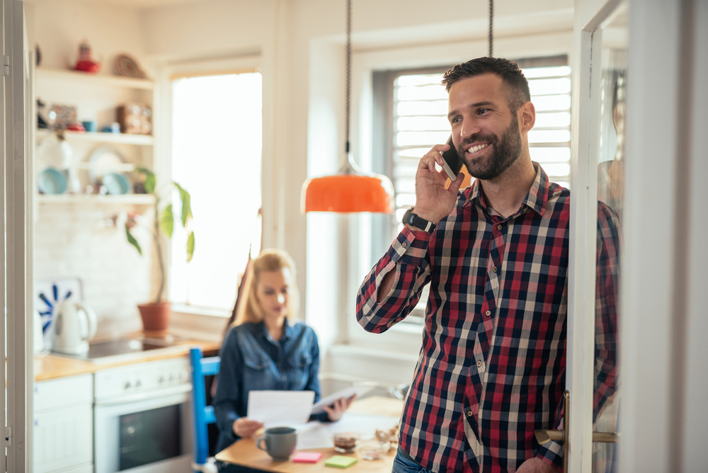 Handsome man smiling while talking on the phone to his HVAC contractor with his wife